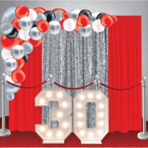 Our Birthday Decor Package 22 has a curtain backdrop, red carpet, stanchions, large organic balloon arch, and two marquee light-up numbers.